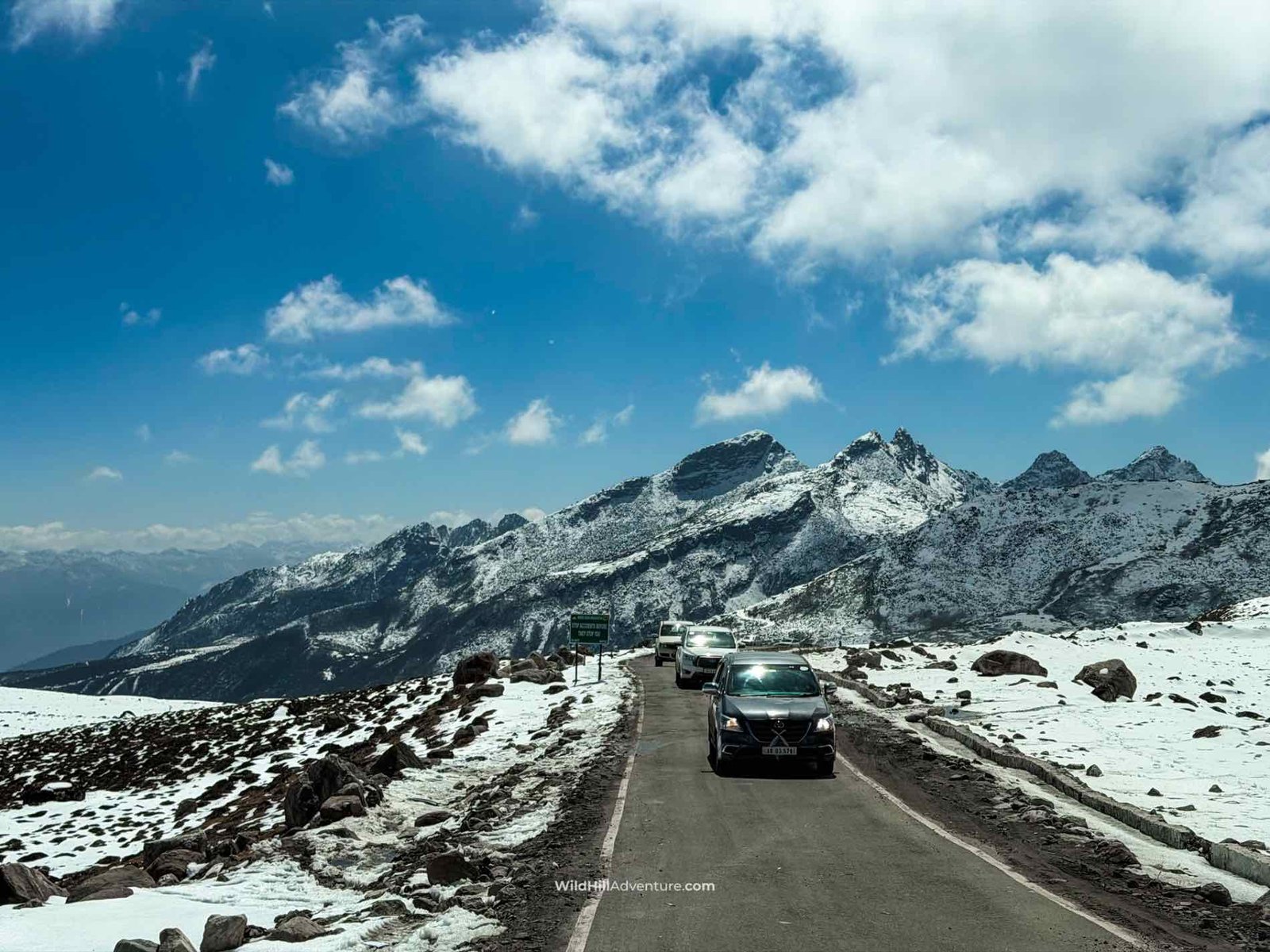 Wild Hill Adventure Snow-covered mountain road in Tawang, Arunachal Pradesh, with vehicles driving through a winter landscape.
